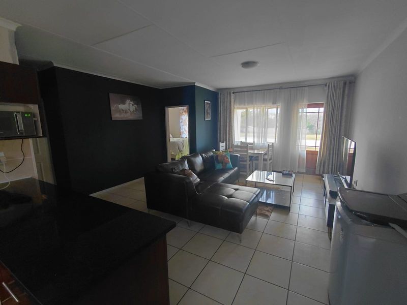Open-plan living area featuring tiled flooring, a kitchen with granite countertops, and direct access to an outdoor space through a sliding door.