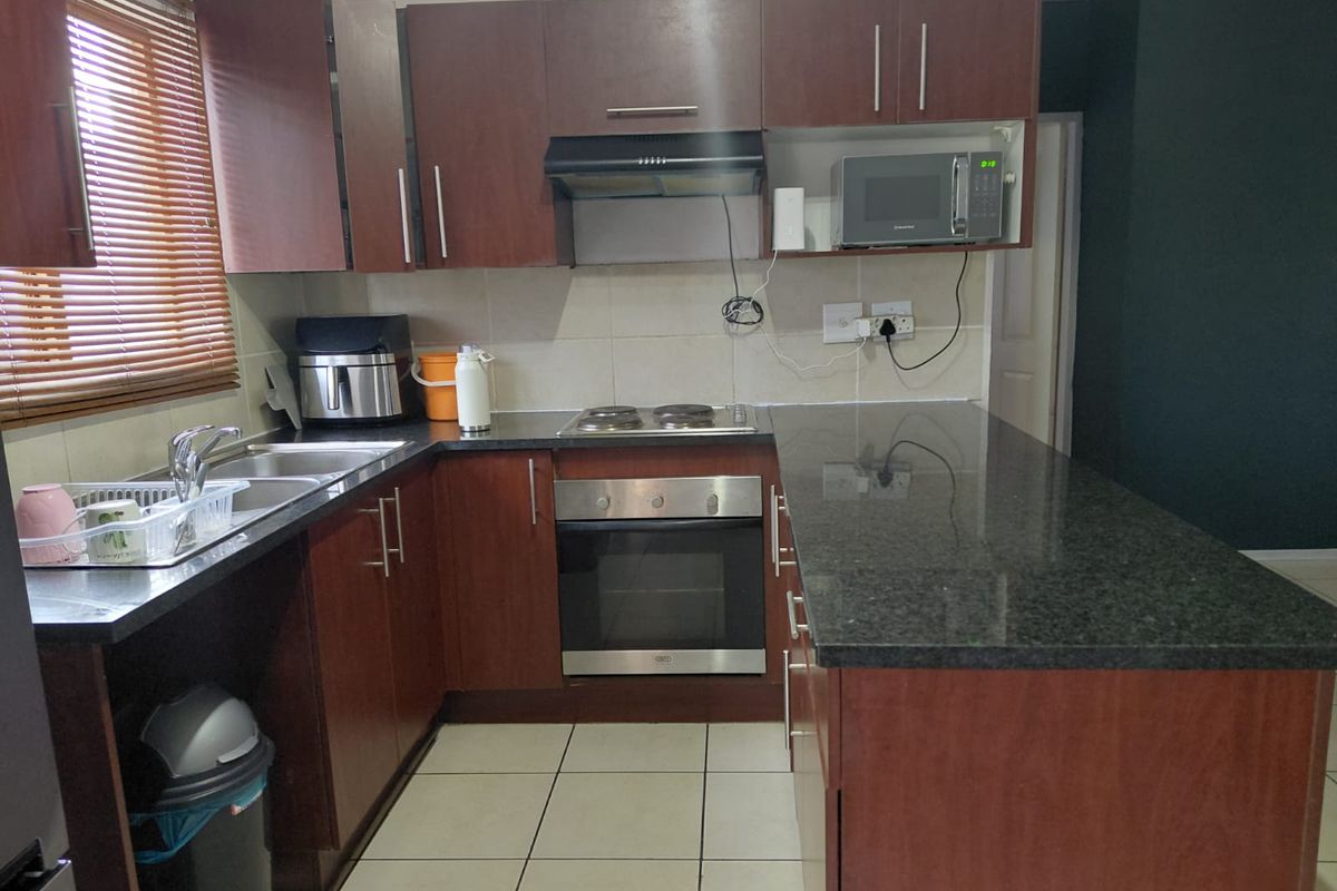 Functional kitchen featuring dark wood cabinetry, granite countertops, built-in oven, electric hob, and tiled flooring with a breakfast bar extension.