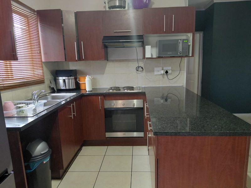 Functional kitchen featuring dark wood cabinetry, granite countertops, built-in oven, electric hob, and tiled flooring with a breakfast bar extension.