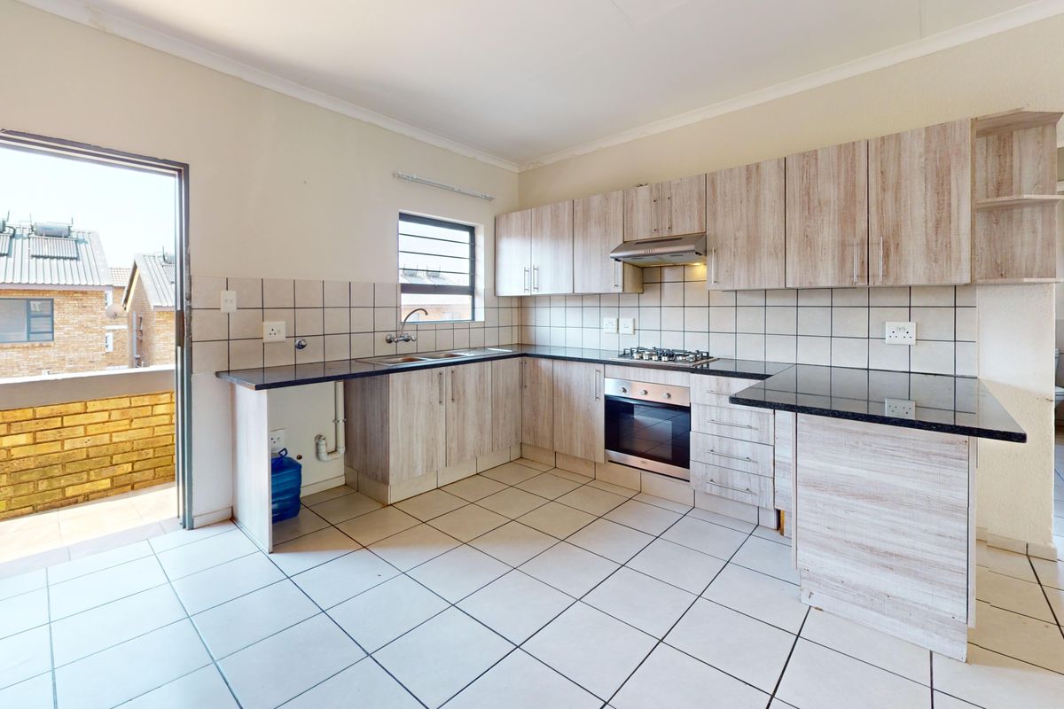 A functional kitchen featuring light wood-finish cabinetry, granite countertops, built-in oven and hob, and direct access to an outdoor balcony area.