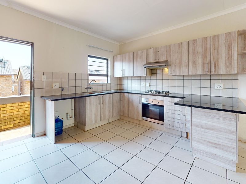 A functional kitchen featuring light wood-finish cabinetry, granite countertops, built-in oven and hob, and direct access to an outdoor balcony area.