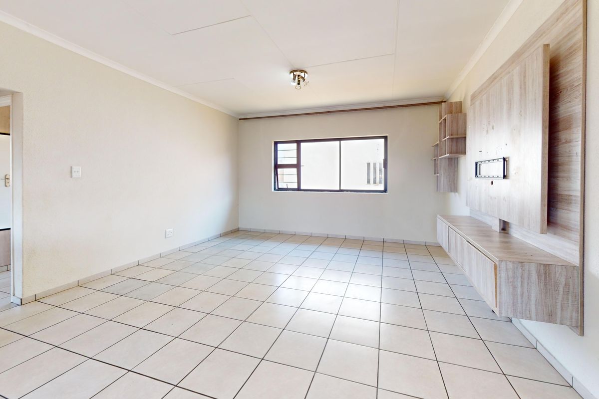 A bright, empty living room featuring neutral tiled flooring and a built-in wooden media console unit.