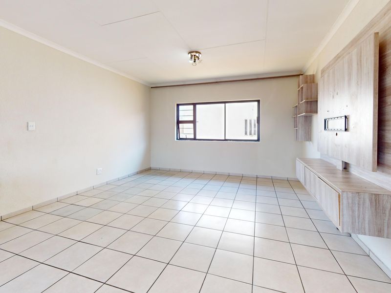A bright, empty living room featuring neutral tiled flooring and a built-in wooden media console unit.