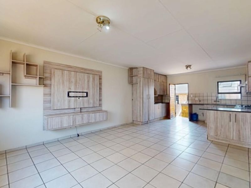Spacious open-plan living and kitchen area featuring light wood-look cabinetry, tiled flooring, and a built-in media unit, offering a functional and versatile layout.