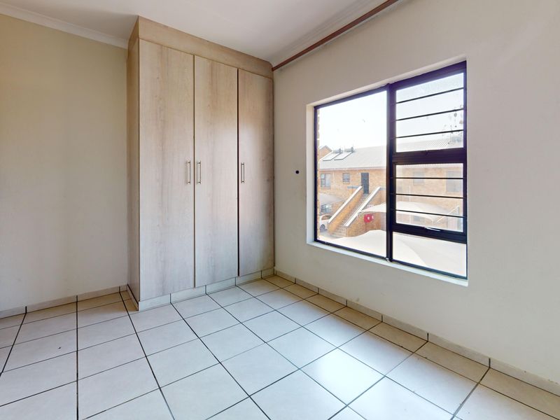A bright, empty bedroom featuring neutral tiled flooring and built-in wooden cupboards, offering a clean and versatile space.