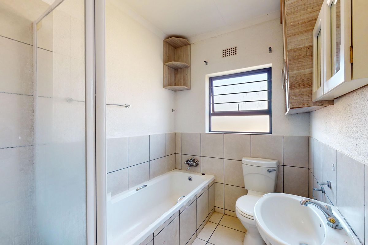 A functional bathroom featuring a bathtub, separate shower enclosure, pedestal basin, and wall-mounted storage cabinetry with neutral tiled finishes.
