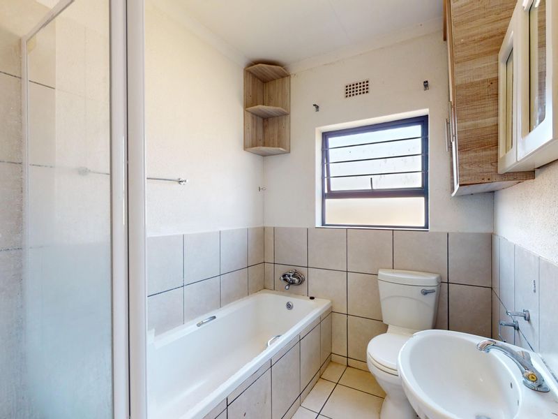 A functional bathroom featuring a bathtub, separate shower enclosure, pedestal basin, and wall-mounted storage cabinetry with neutral tiled finishes.