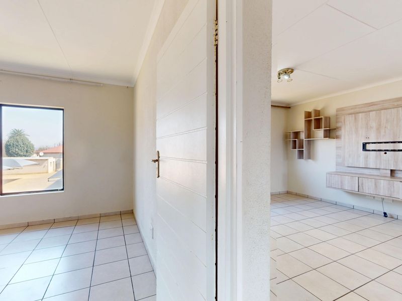 An empty living area featuring tiled flooring, a built-in media unit with shelving, and a window with security bars.