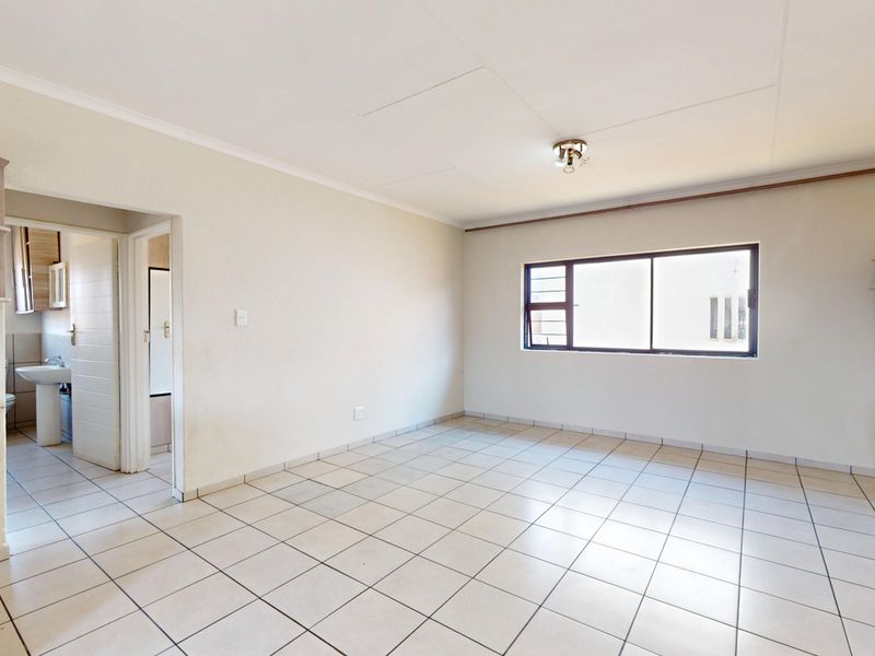 An open-plan living area featuring neutral tiled flooring, built-in cabinetry, and a sliding window, providing a clean and versatile space.