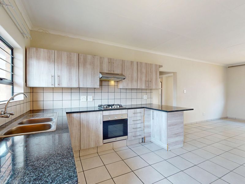 Open-plan kitchen featuring light wood-grain cabinetry, granite countertops, gas hob, and tiled flooring, flowing into an adjacent living area.