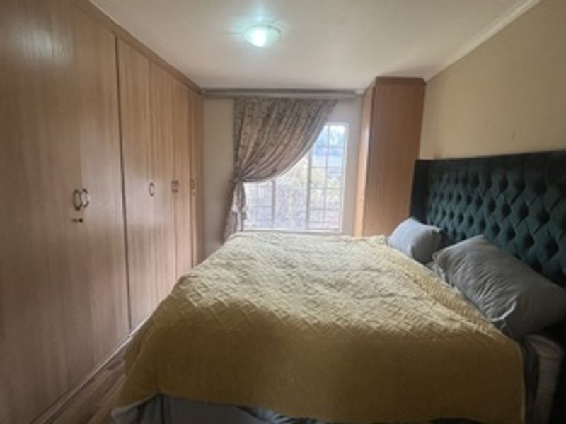 A bedroom featuring extensive built-in wooden cupboards and a window with natural light, providing functional storage and a comfortable living space.