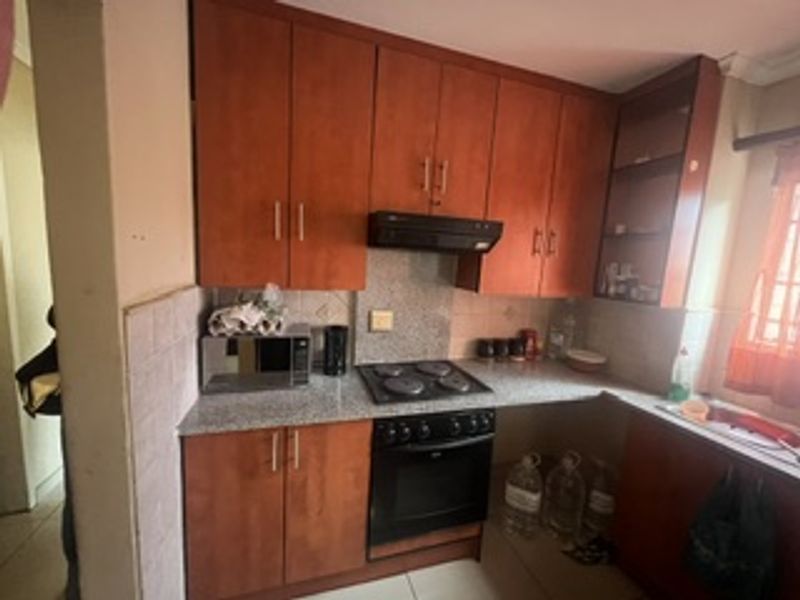 A functional kitchen featuring wooden cabinetry, granite countertops, a built-in oven, electric hob, and an integrated extractor fan.