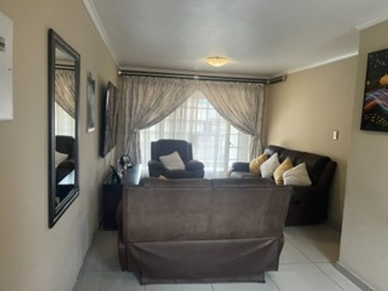 A comfortable living room featuring neutral wall tones, tiled flooring, and large windows dressed with curtains, providing a functional and inviting space.