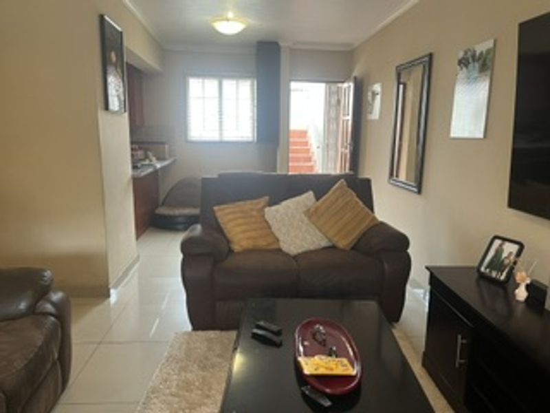 Open plan living area featuring tiled flooring and an integrated kitchen space with built-in cabinetry, leading to an exterior entrance.