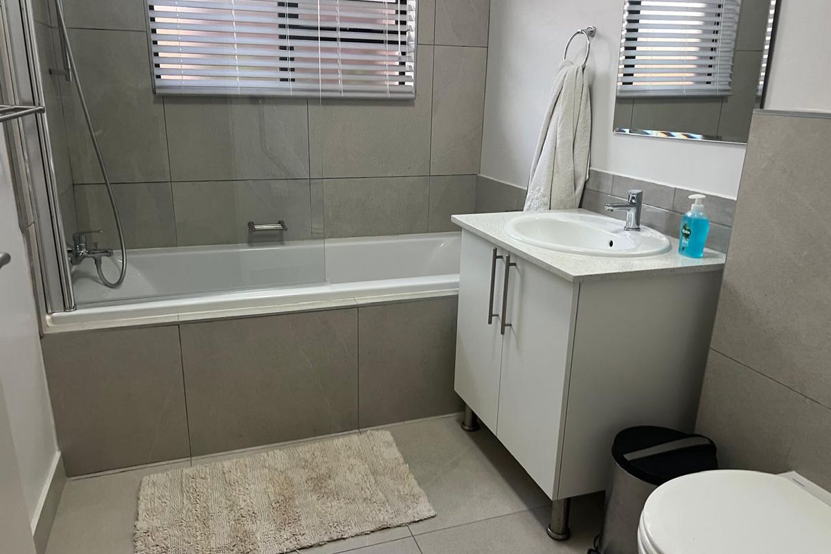 Modern bathroom featuring a built-in bathtub with glass screen, vanity cabinet with basin, and neutral floor-to-ceiling wall tiles.