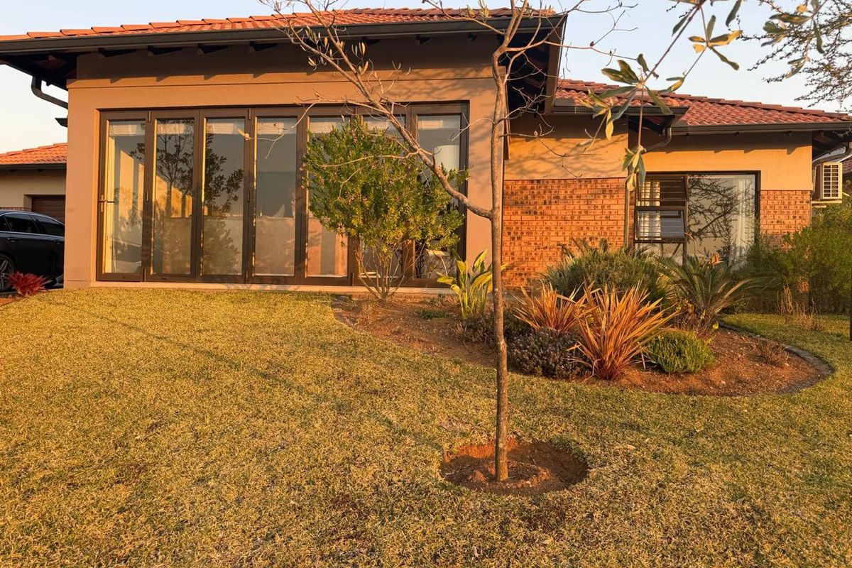 Rear view of a modern house featuring a brick and stucco facade, large aluminium stacker doors, and a well-maintained garden.