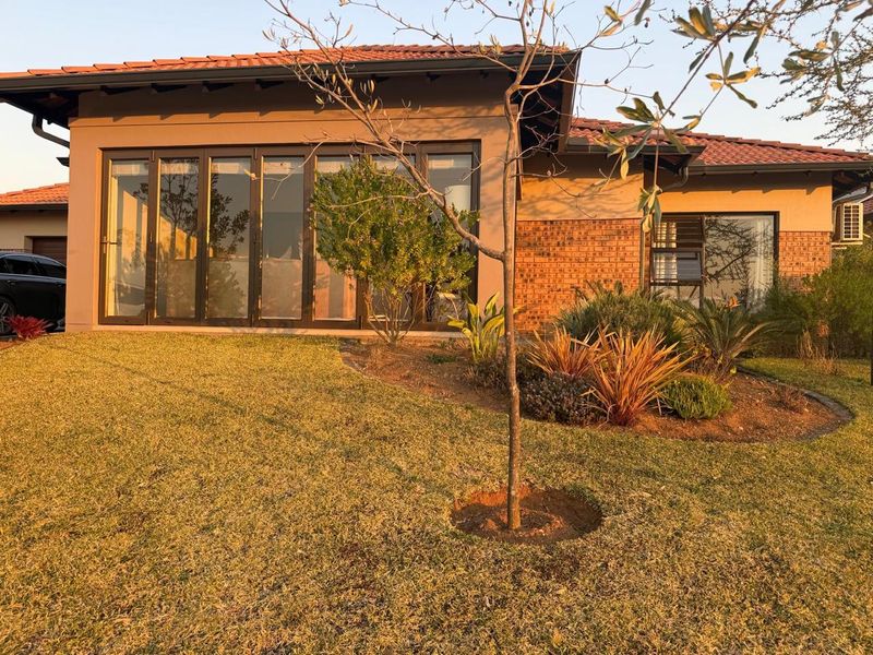 Rear view of a modern house featuring a brick and stucco facade, large aluminium stacker doors, and a well-maintained garden.