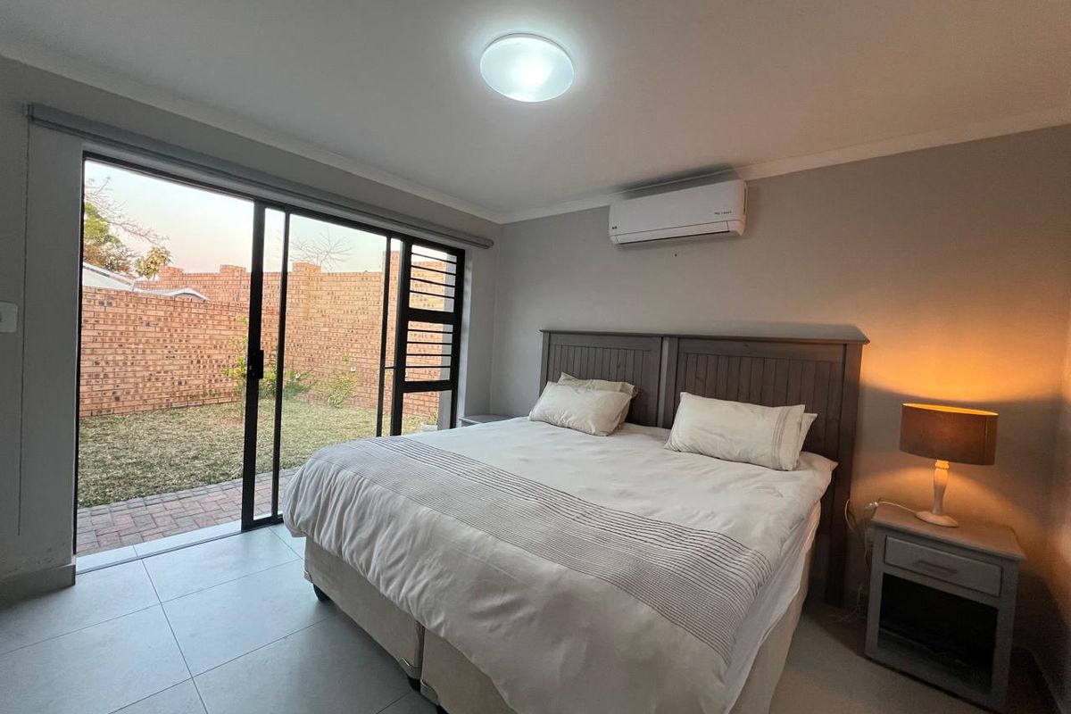 A well-maintained bedroom featuring tiled flooring, a split-system air conditioner, and large sliding glass doors providing direct access to the rear garden.