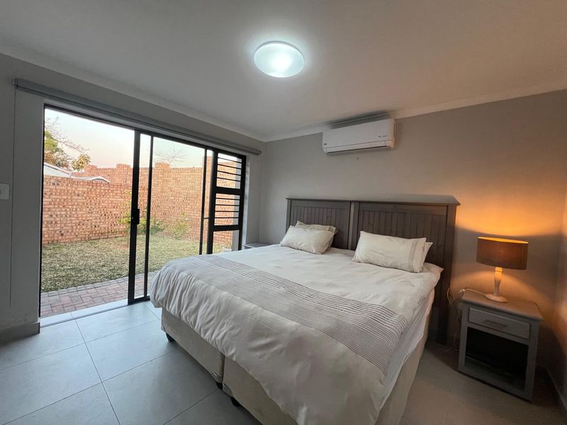 A well-maintained bedroom featuring tiled flooring, a split-system air conditioner, and large sliding glass doors providing direct access to the rear garden.