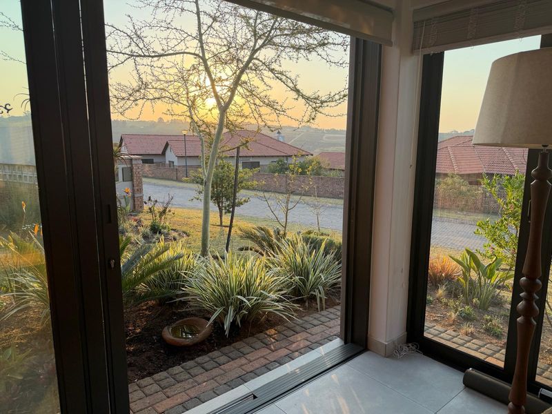 A view from an interior space looking out through large sliding glass doors onto a landscaped garden and residential street at sunset.