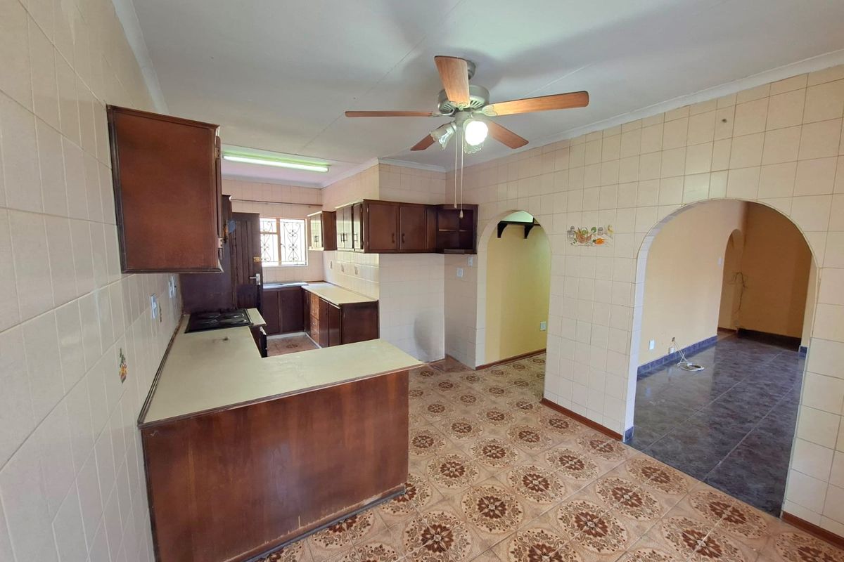 A spacious, dated kitchen featuring built-in wooden cabinetry, tiled surfaces, and an open-plan layout with archway access to adjacent living areas.