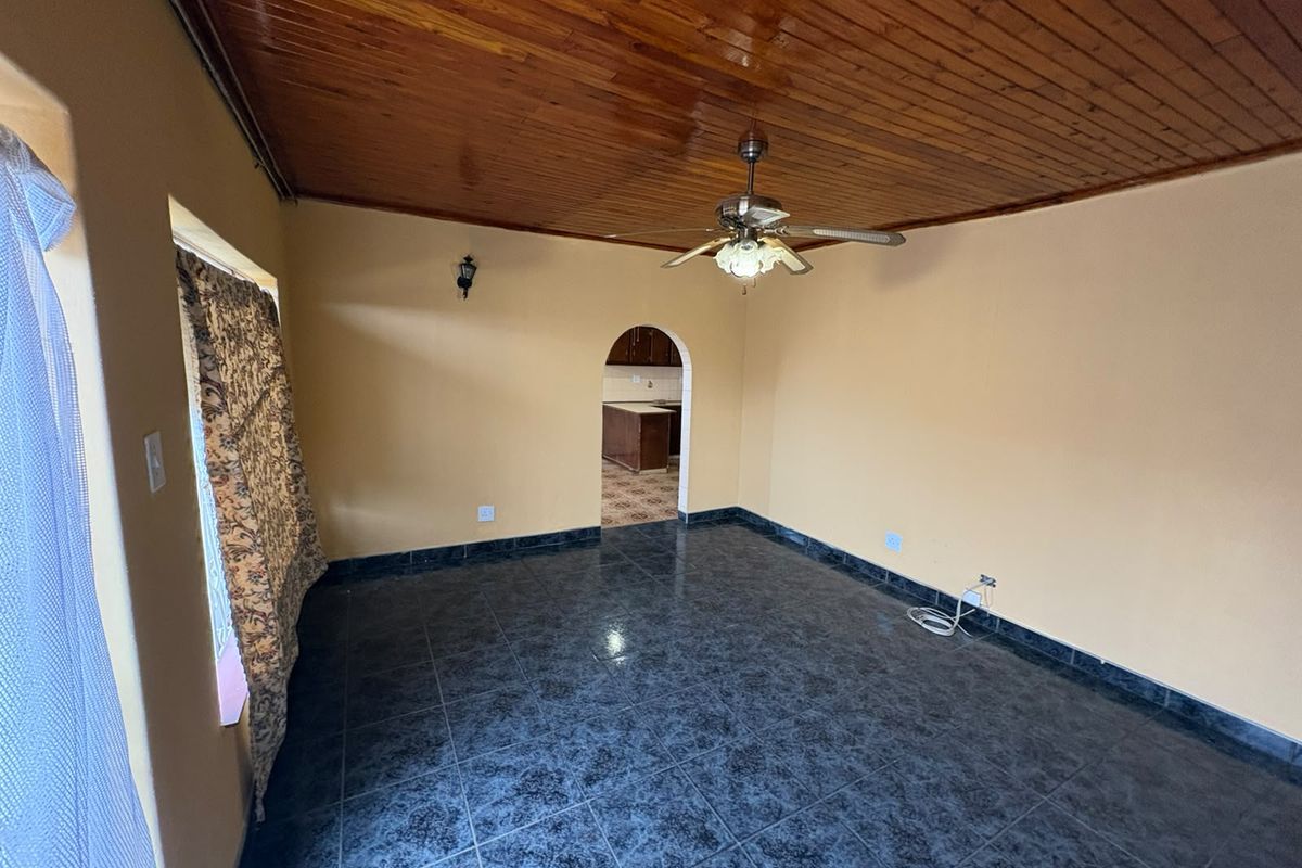 Spacious living area featuring dark tiled flooring, a timber tongue and groove ceiling, and an arched entryway leading to the kitchen.