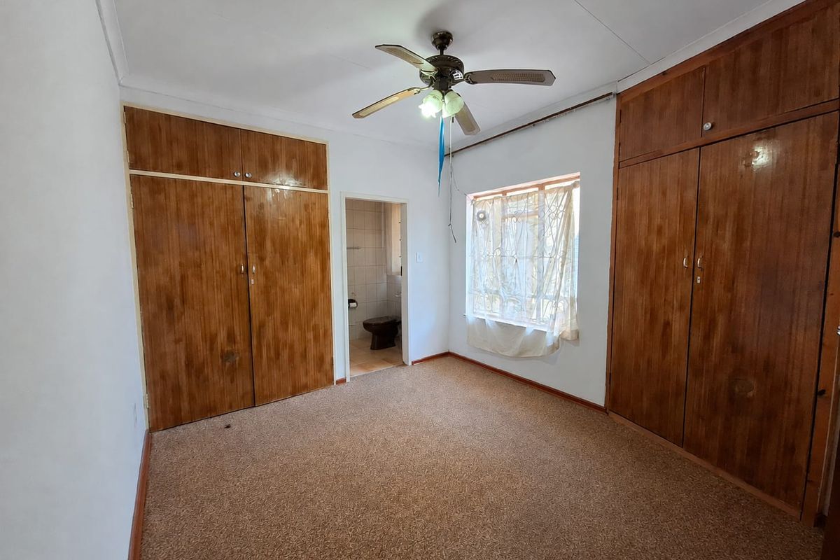 A bedroom featuring built-in wooden cupboards, a ceiling fan, and carpeted flooring, with direct access to an en-suite bathroom.