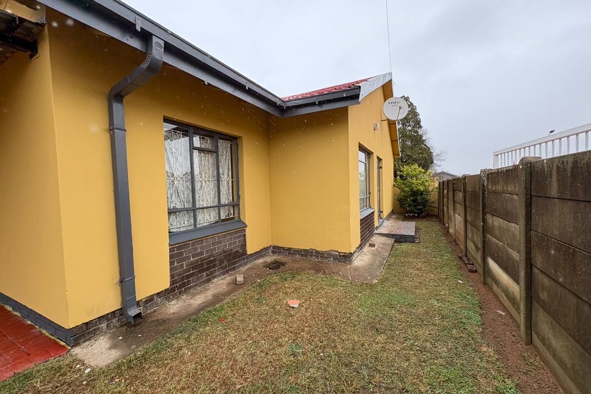 Rear exterior view of the house featuring yellow painted walls, a metal roof, and a precast concrete boundary wall enclosing the garden area.