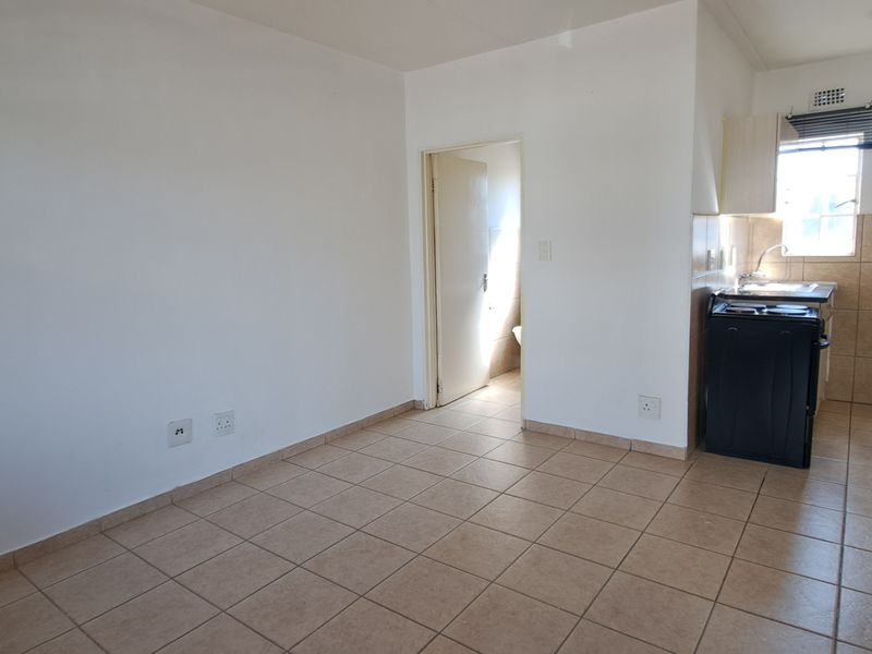 An open-plan living and kitchen area featuring tiled flooring, neutral walls, and a functional kitchen space with built-in cabinetry and a stove.