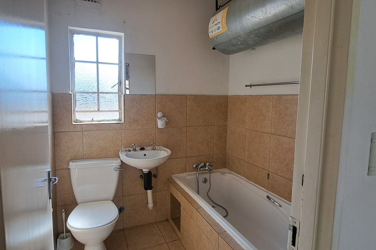 A functional bathroom featuring a bathtub, pedestal basin, and toilet, with tiled finishes and an exposed geyser unit.