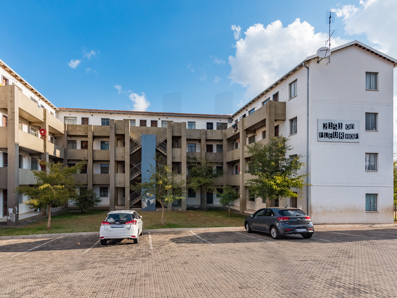 Front elevation of the 2151 on Fleurhof apartment complex, featuring a paved parking area and multi-story residential building with external stairwells.