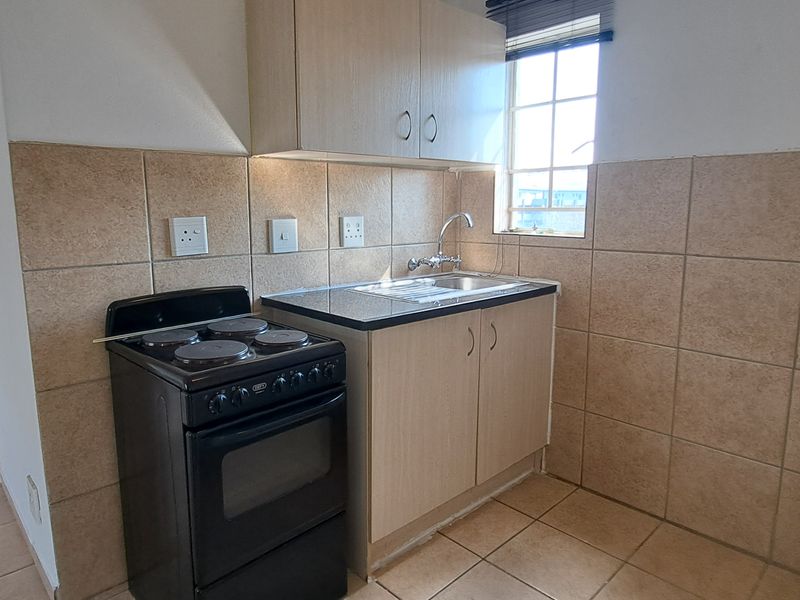 Compact kitchen featuring built-in cabinetry, laminate countertops, a stainless steel sink, tiled backsplash, and a freestanding stove.