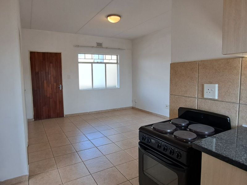 An open-plan living and kitchen area featuring tiled flooring, built-in cabinetry with granite countertops, and an electric stove.