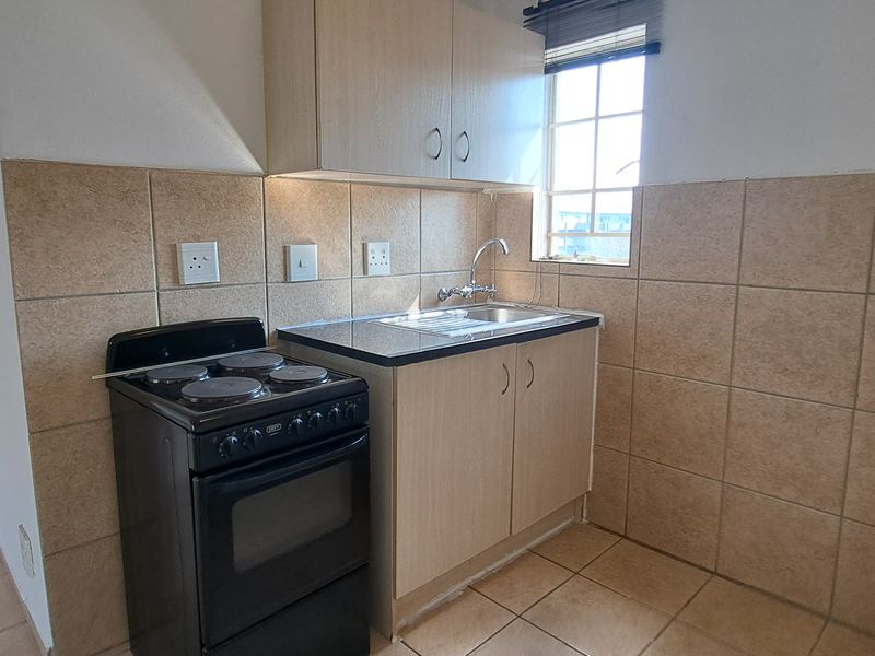 Compact kitchen featuring light wood-finish cabinetry, tiled backsplash, stainless steel sink, and a freestanding stove with tiled flooring throughout.
