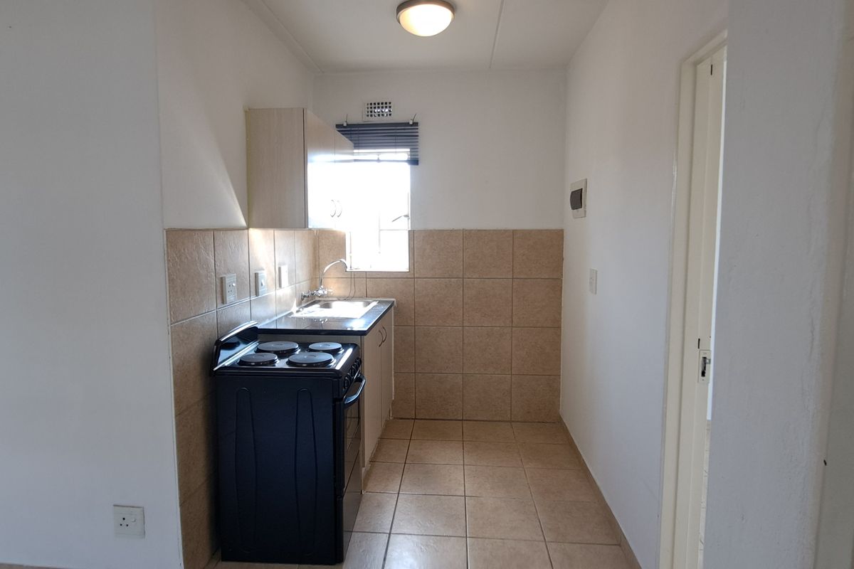 A compact, functional kitchen featuring tiled splashbacks, tiled flooring, built-in cabinetry, and a freestanding stove.