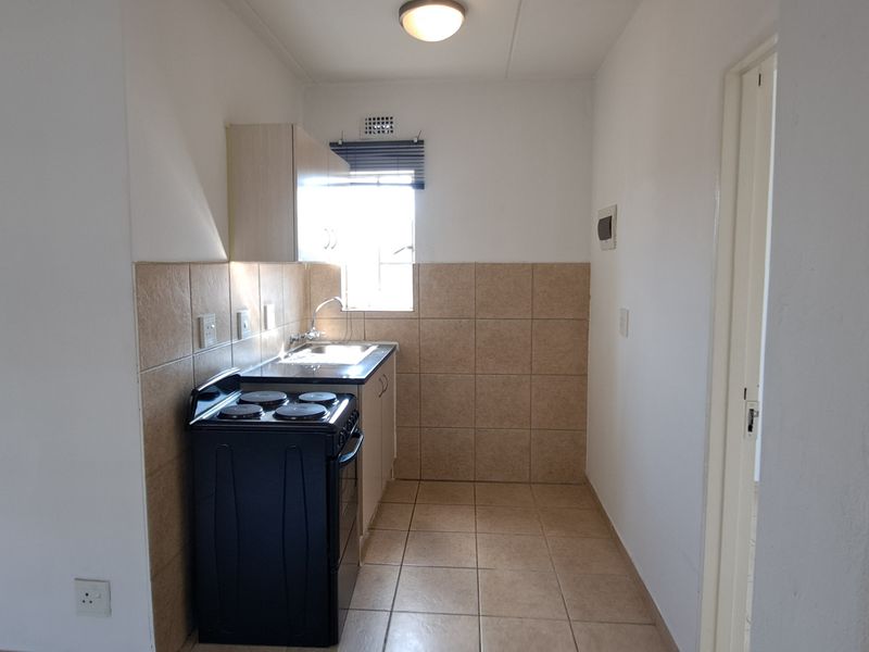 A compact, functional kitchen featuring tiled splashbacks, tiled flooring, built-in cabinetry, and a freestanding stove.