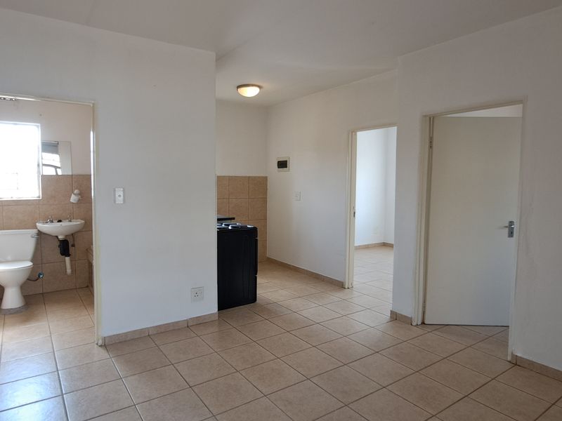 An open-plan living area featuring neutral tiled flooring, white walls, and direct access to an adjoining bathroom and additional rooms.
