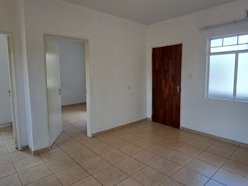 An empty living area featuring neutral tiled flooring, a timber door, and large windows providing natural light, ready for personalization.