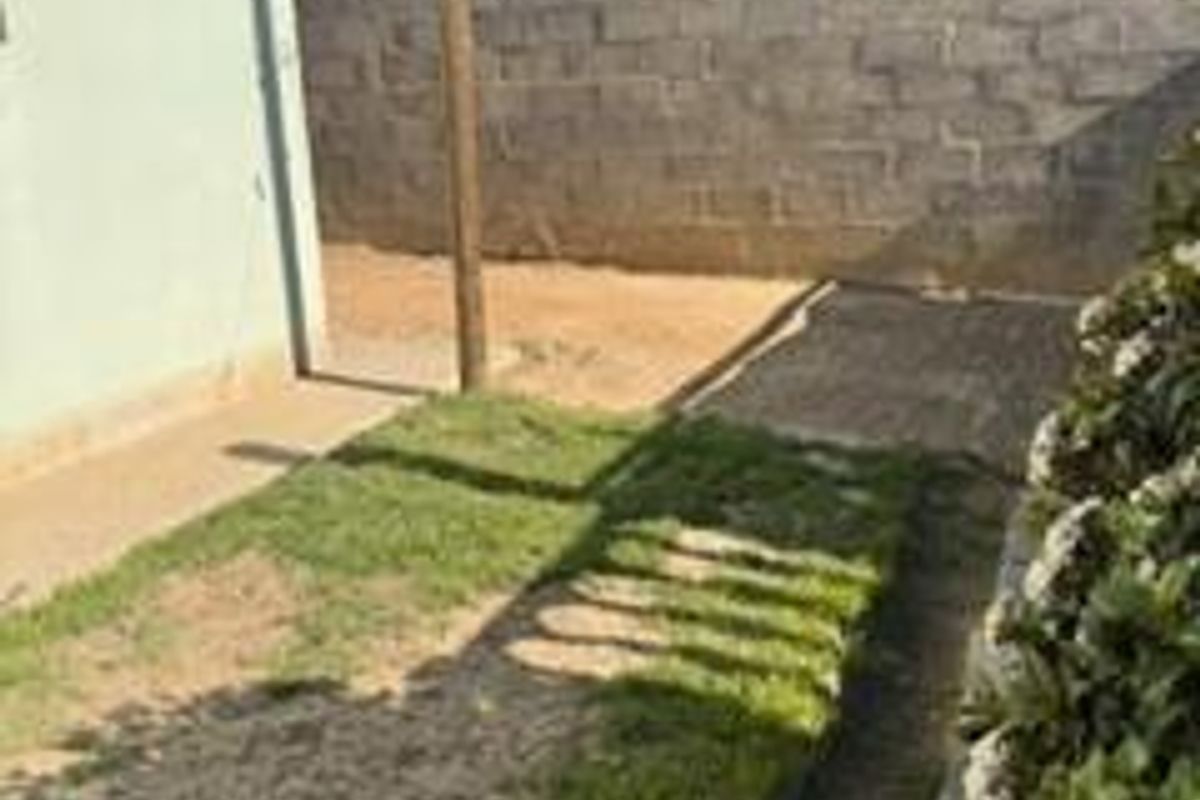 A rear exterior view showing a small lawn area, paved walkway, and concrete block boundary wall.