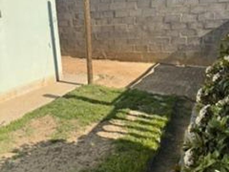 A rear exterior view showing a small lawn area, paved walkway, and concrete block boundary wall.