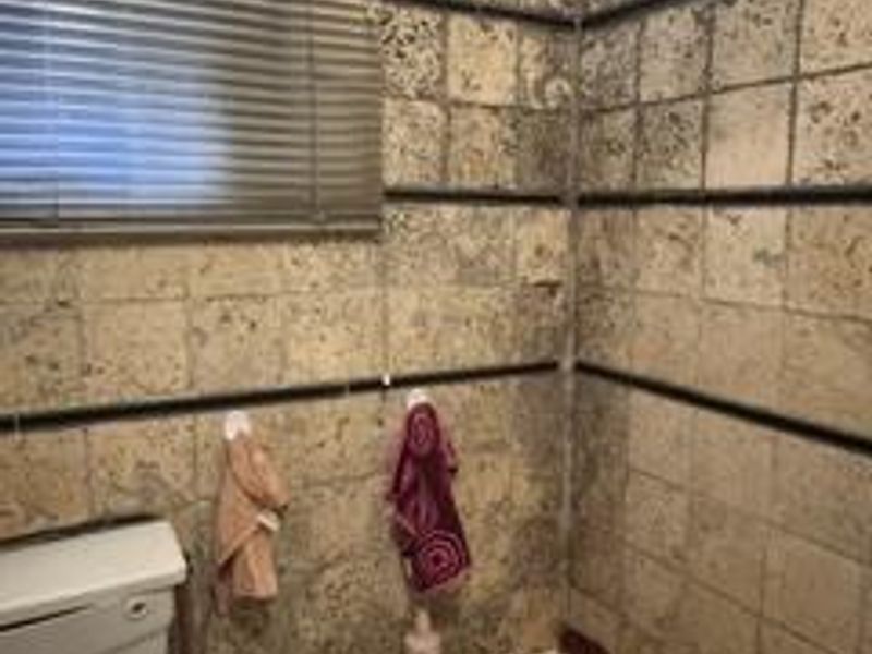 A bathroom featuring a bathtub, toilet cistern, and dated textured wall tiles with venetian blinds.