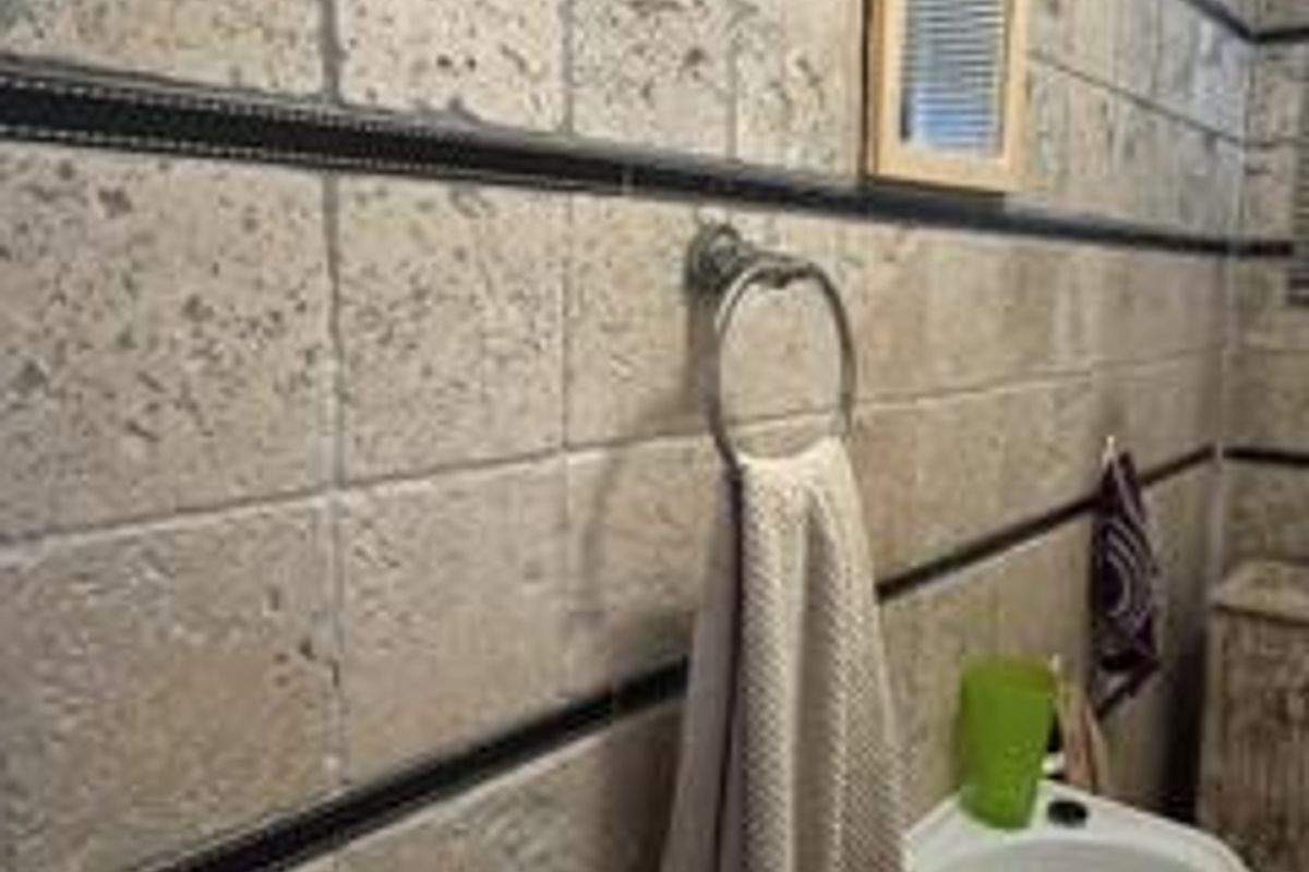 A bathroom featuring textured travertine wall tiles with decorative dark inlay borders and a wall-mounted basin.
