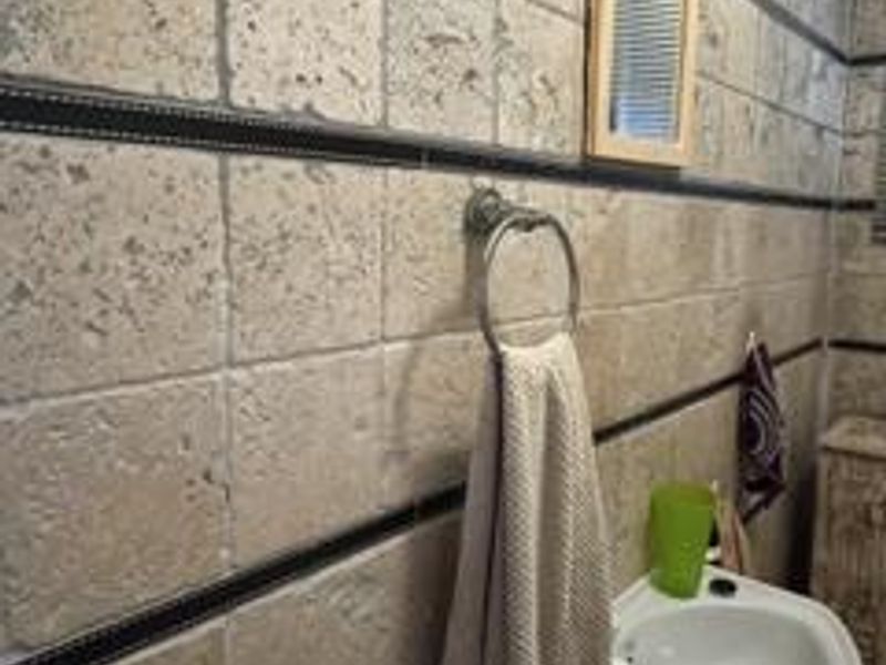 A bathroom featuring textured travertine wall tiles with decorative dark inlay borders and a wall-mounted basin.