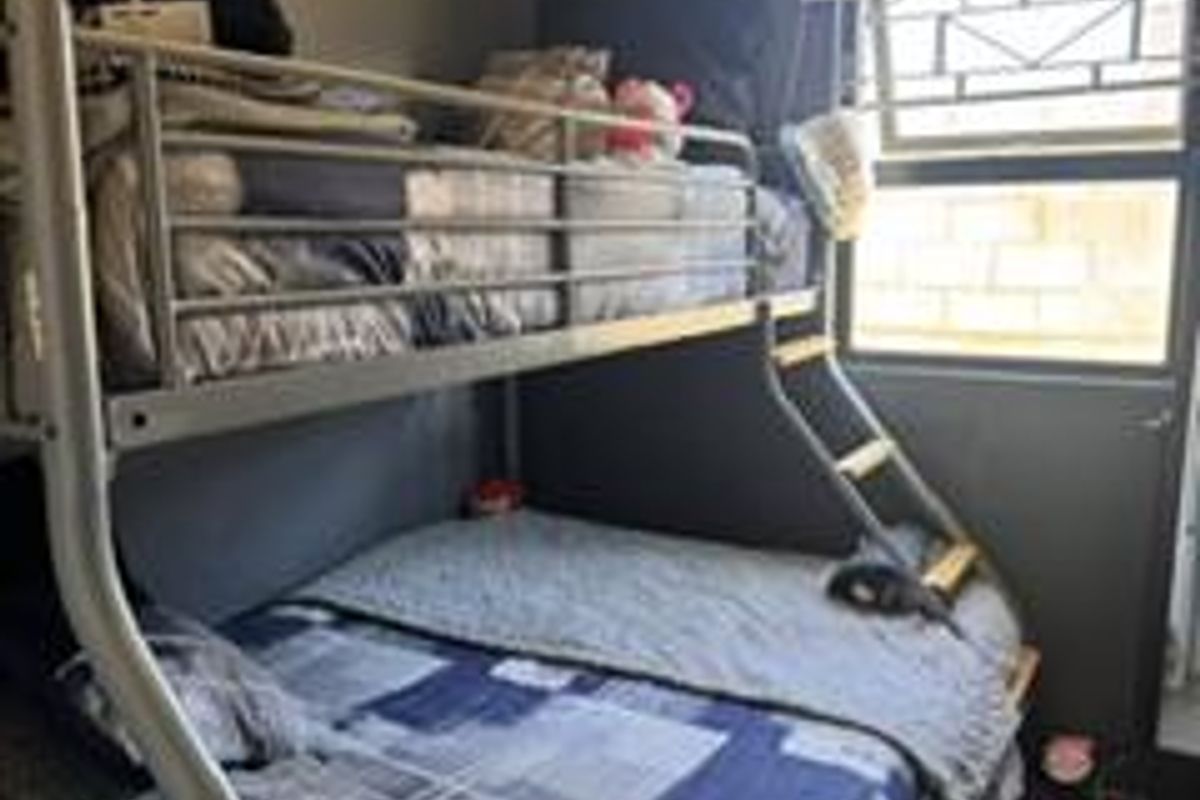 A compact bedroom featuring a bunk bed, security bars on the window, and neutral wall finishes.