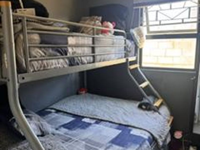 A compact bedroom featuring a bunk bed, security bars on the window, and neutral wall finishes.