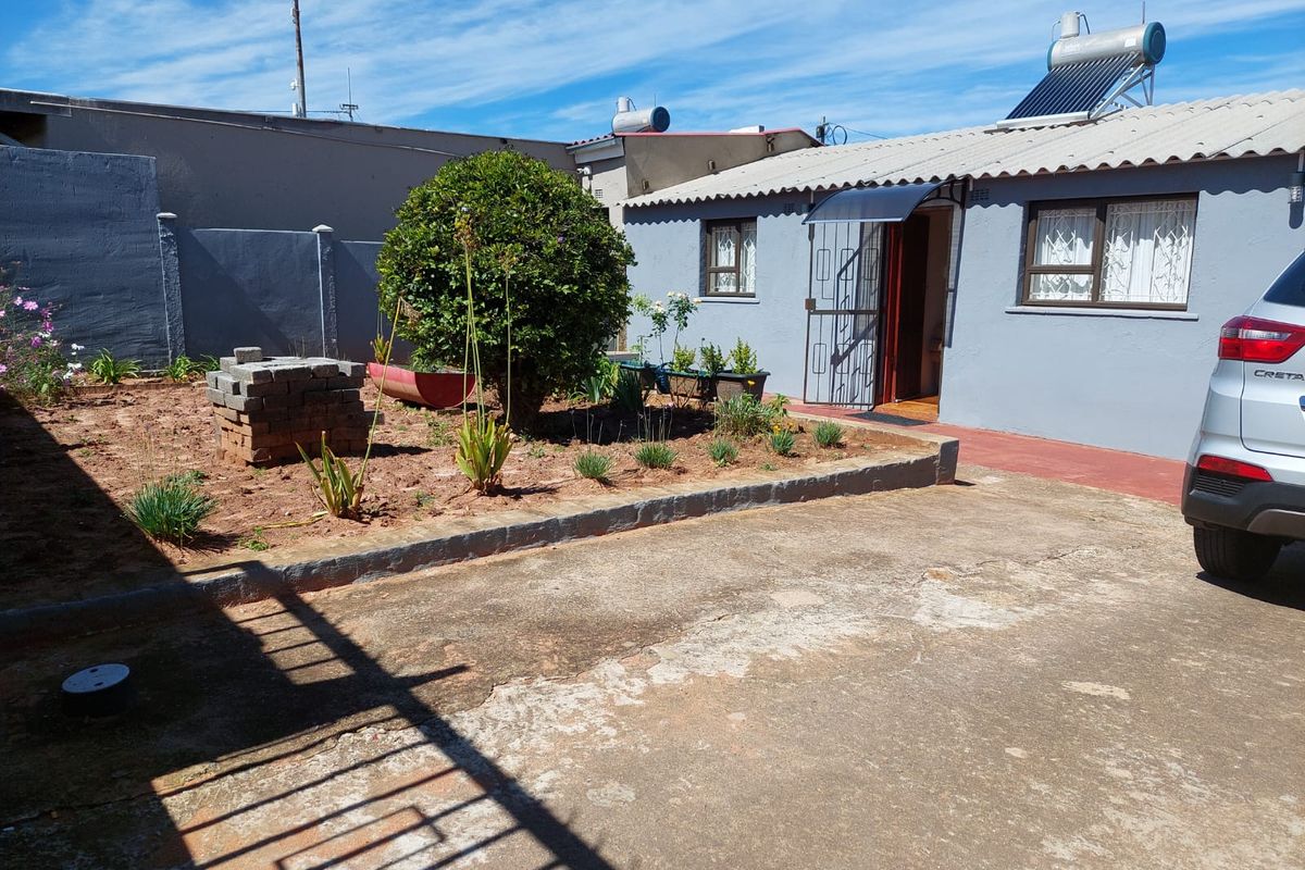 Rear exterior view of the house featuring a concrete driveway, solar water heater, and a small garden area with boundary walling.
