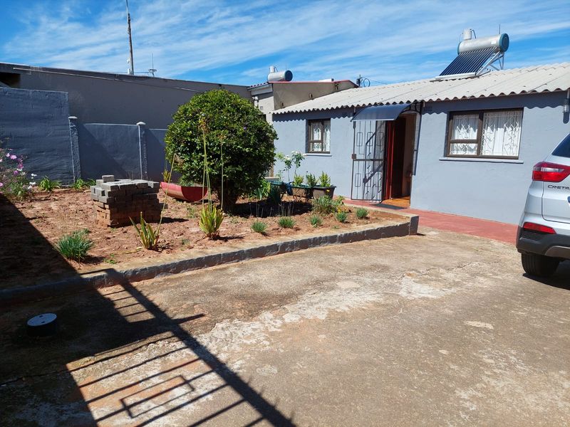 Rear exterior view of the house featuring a concrete driveway, solar water heater, and a small garden area with boundary walling.