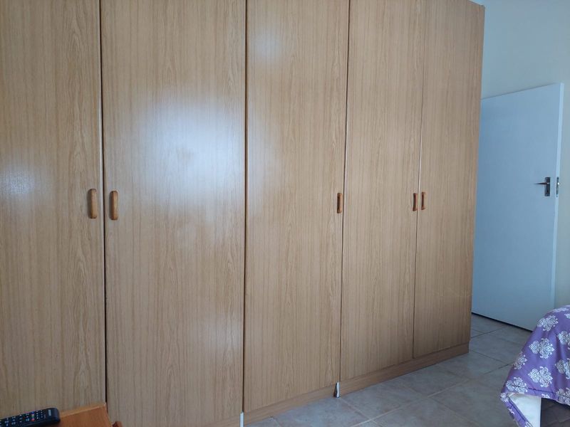 A bedroom featuring a large, light wood-grain built-in wardrobe and neutral tiled flooring.