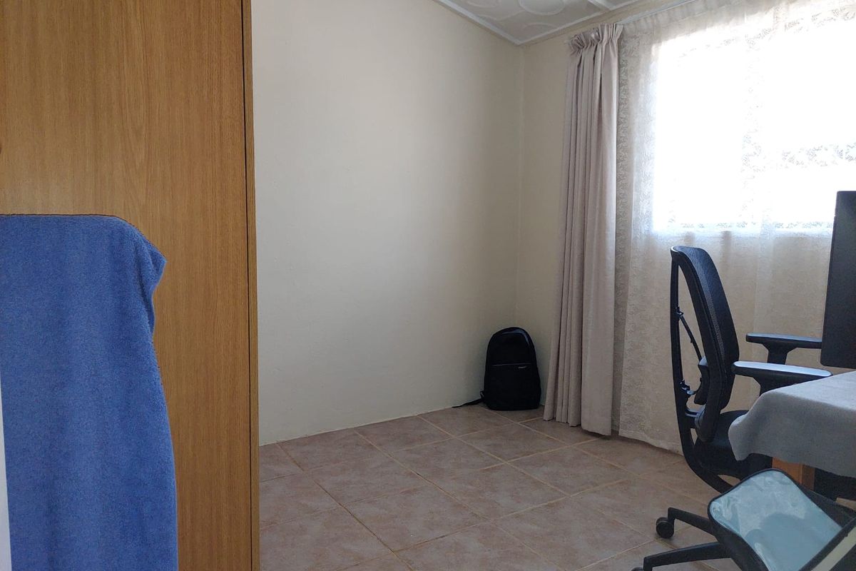 A functional bedroom featuring tiled flooring, a built-in wardrobe, and natural light through a window with installed curtain tracks.