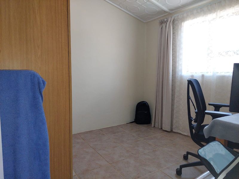 A functional bedroom featuring tiled flooring, a built-in wardrobe, and natural light through a window with installed curtain tracks.